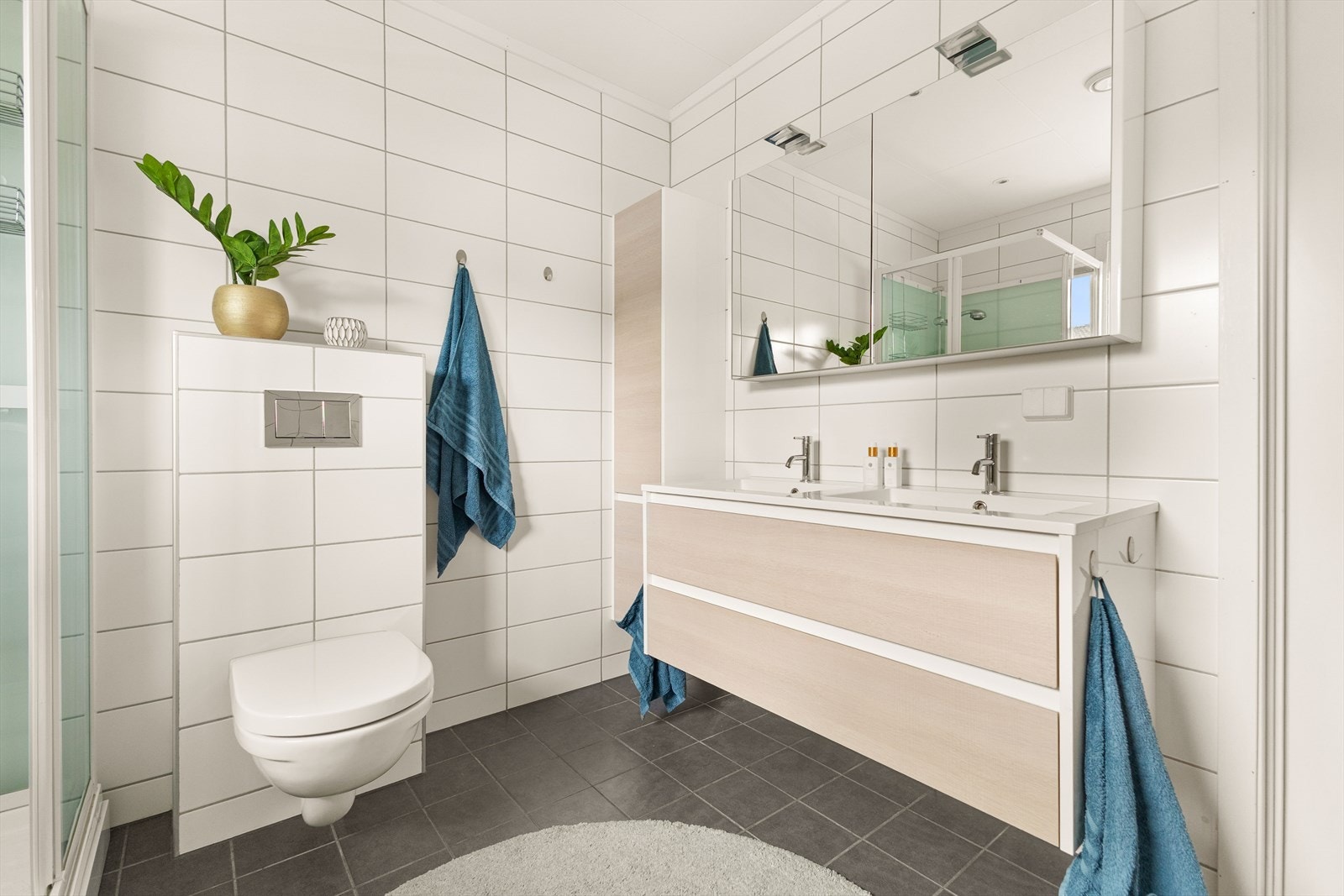 Baderommet er utstyrt med dobbel servantinnredning, speilskap, oppbevaringsskap, vegghengt toalett, dusjkabinett samt opplegg for vaskemaskin. Avtrekk via balansert ventilasjon. Galleribilde