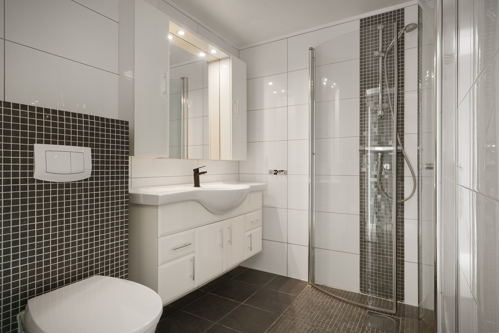 Flislagt bad med dusjnisje, vegghengt toalett og servant på innredning Galleribilde