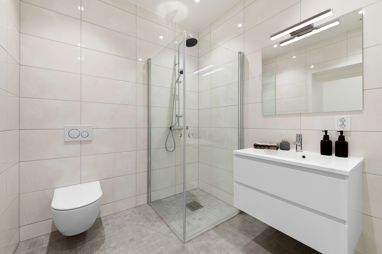 Dusjhjørne med glassvegger og vegghengt dusjarmatur med hånddusj og regndusj.. Vegghengt toalett. Innredning med servant med ett-greps armatur og speil med overlys over servant Galleribilde