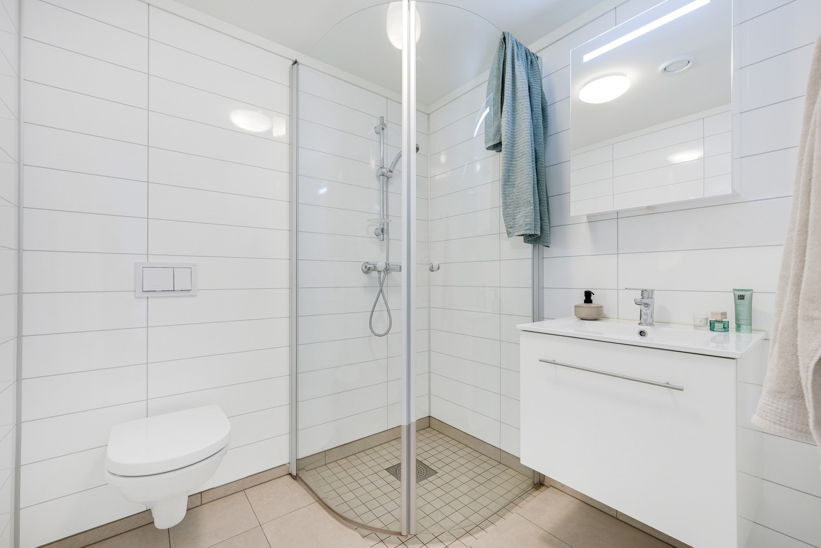 I 1. etasje er det enda et bad med flislagte gulv og baderomsplater på veggene. Her er det en nedsenket dusjnisje. Enkel innredning med overskap m/speil og en servant med skuff. Galleribilde