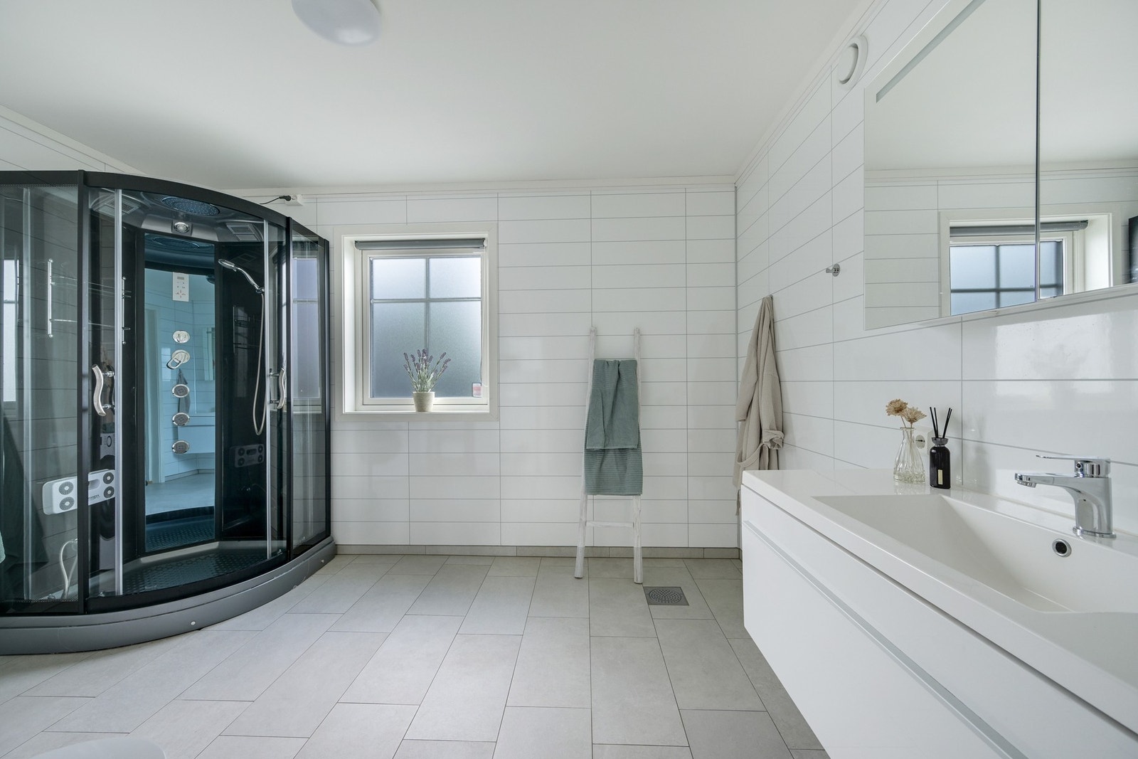 Badet inneholder et stort dusjkabinett, en pen innredning med over- og underskap med servant og opplegg for vaskemaskin. Her er det også god plass til tørketrommel. Galleribilde