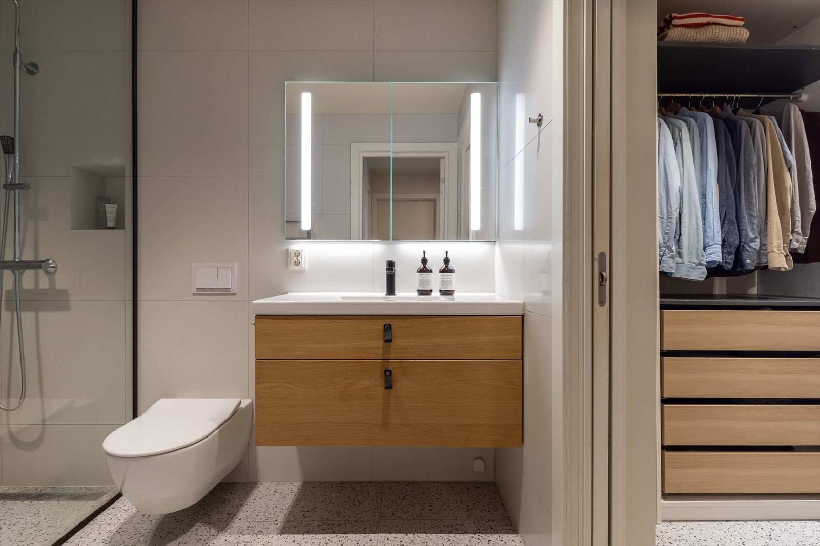 Pent helfliset baderom med downlights og utstyrt med servant i skap, vegghengt toalett og dusjhjørne Galleribilde