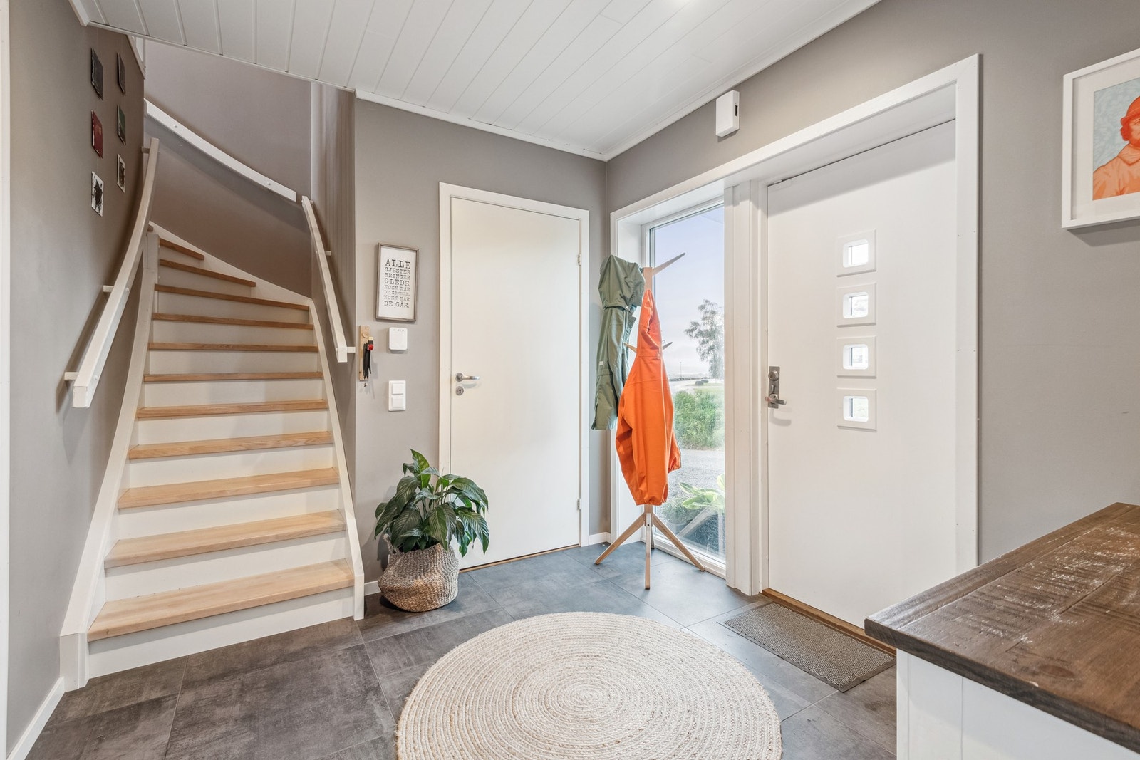 Innbydende gang i 1. etasje med flislagt gulv og stort vindu. Praktisk med en liten bod samt et vaskerom rett innenfor inngangsdøra. Galleribilde