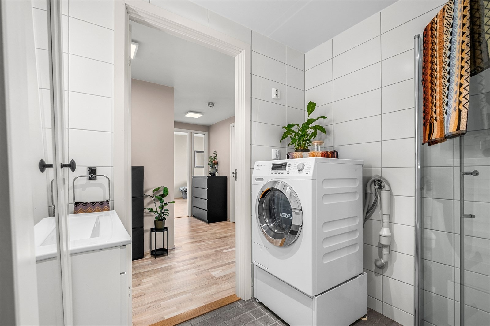 Badet byr på servant, dusjhjørne med innfellbare glassdører og dusjgarnityr montert på vegg, vegghengt toalett og opplegg for vaskemaskin. Galleribilde