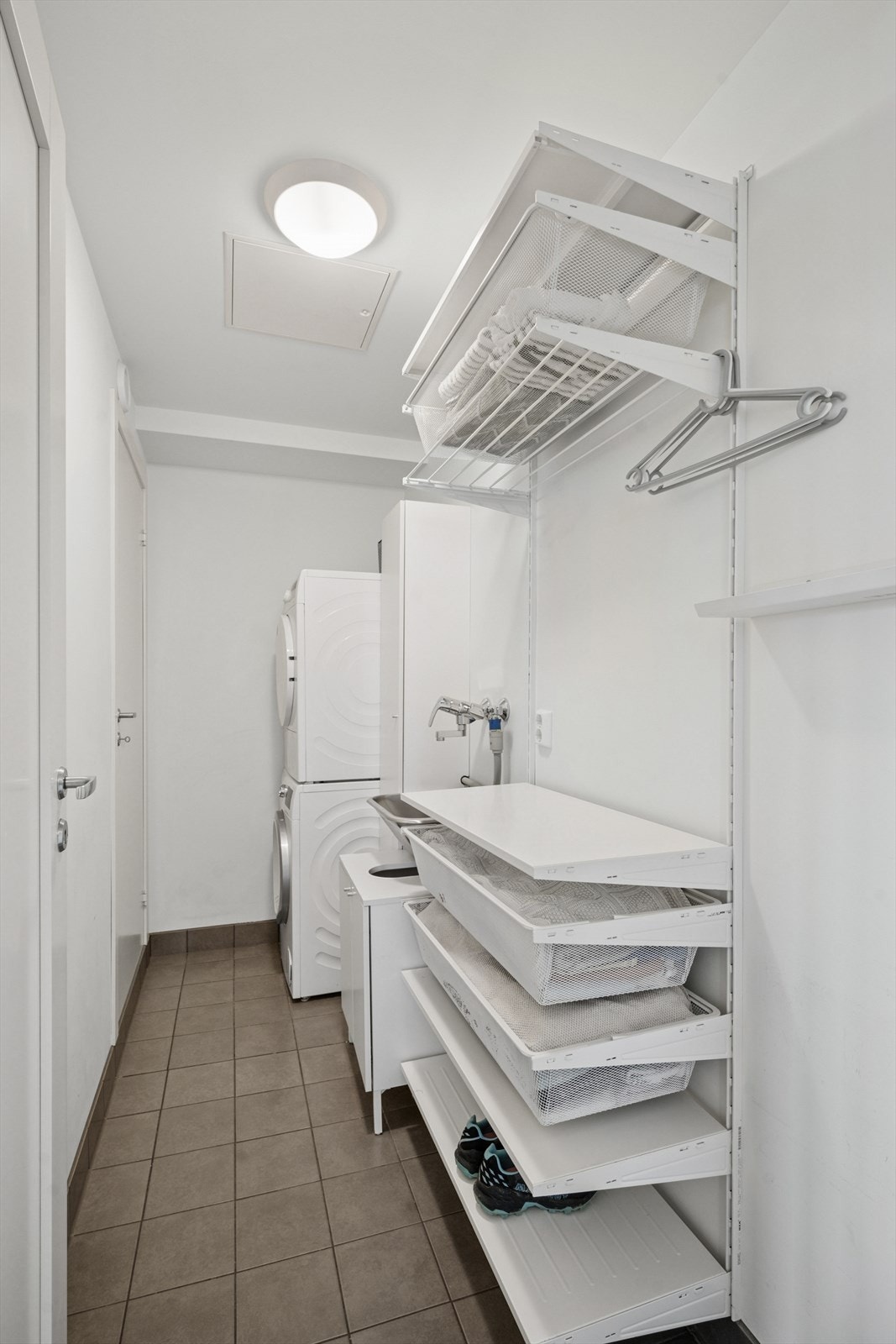 Separat vaskerom med inngang til teknisk rom. Flislagt gulv og hyller montert på vegg, utslagsvask i rustfritt stål og opplegg for vaskemaskin Galleribilde