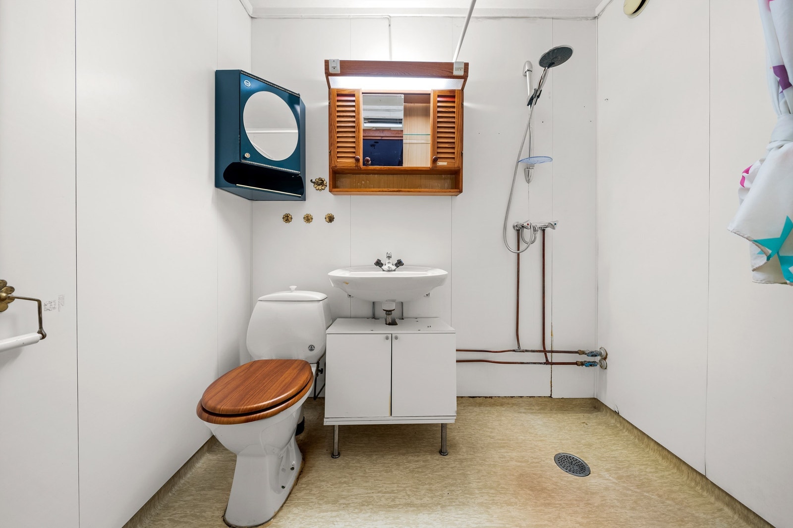 Baderommet har belegg på gulv, våtromsplater på vegger, servant med skapinnredning, speilskap, toalett og dusj direkte på gulv. Galleribilde