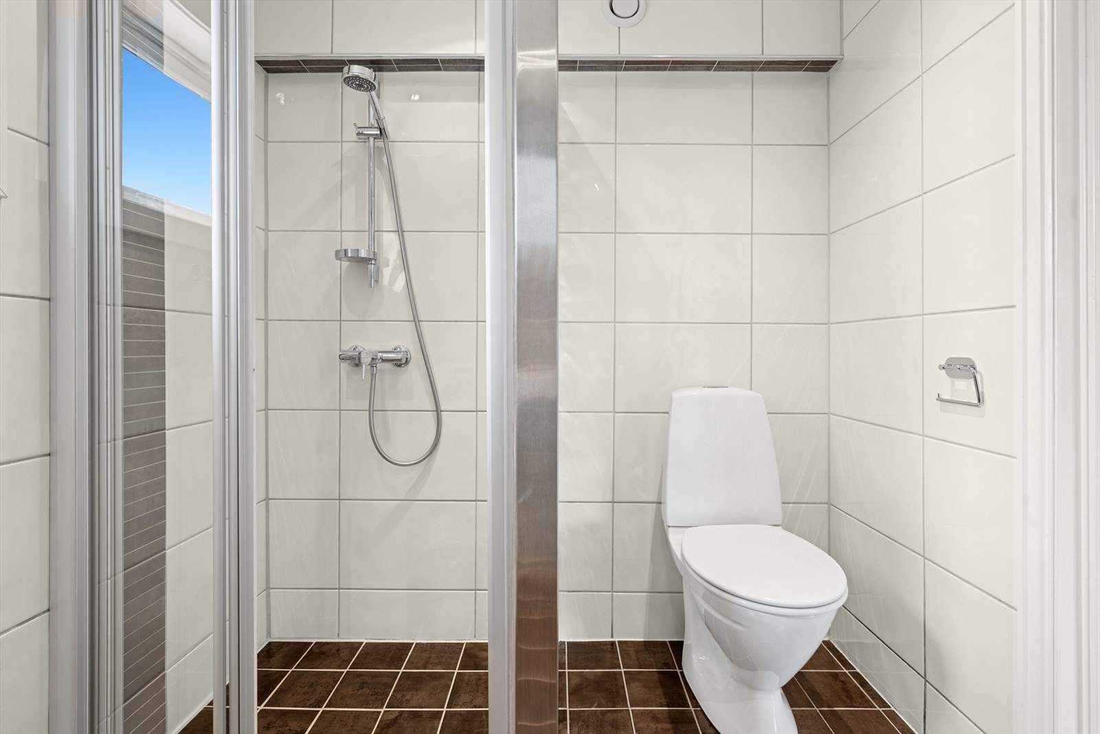 Flislagt baderom med dusjsone og glassvegger. Pent baderomsinteriør, klosett og opplegg for vaskemaskin. Galleribilde