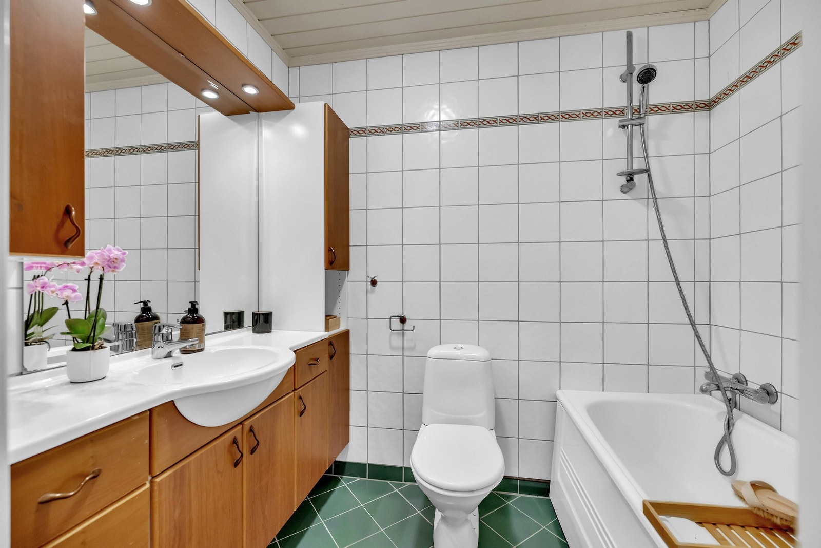 Flislagt baderom fra byggeåret med gulvvarme, vegghengt servantinnredning, gulvstående toalett og badekar med hånddusj. Galleribilde