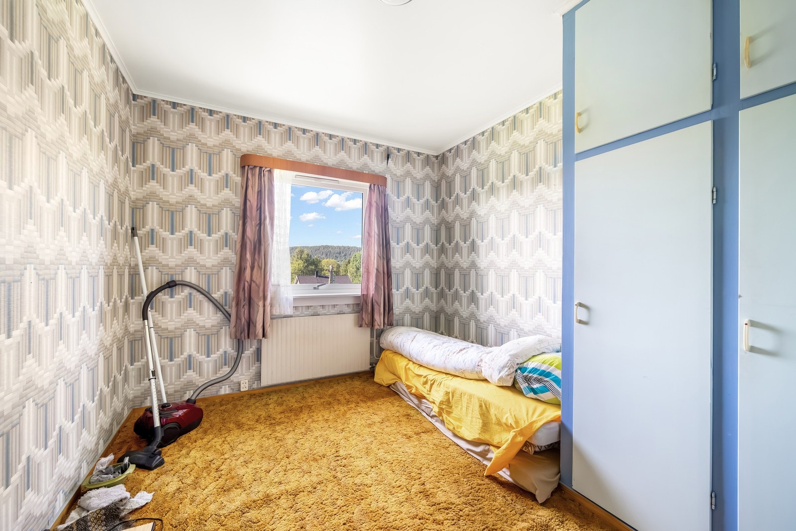 Soverom 1 med plassbygde garderobeskap og panelovn under vinduet. Vindu mot nordvest - så her slipper ikke morgensolen inn. Galleribilde