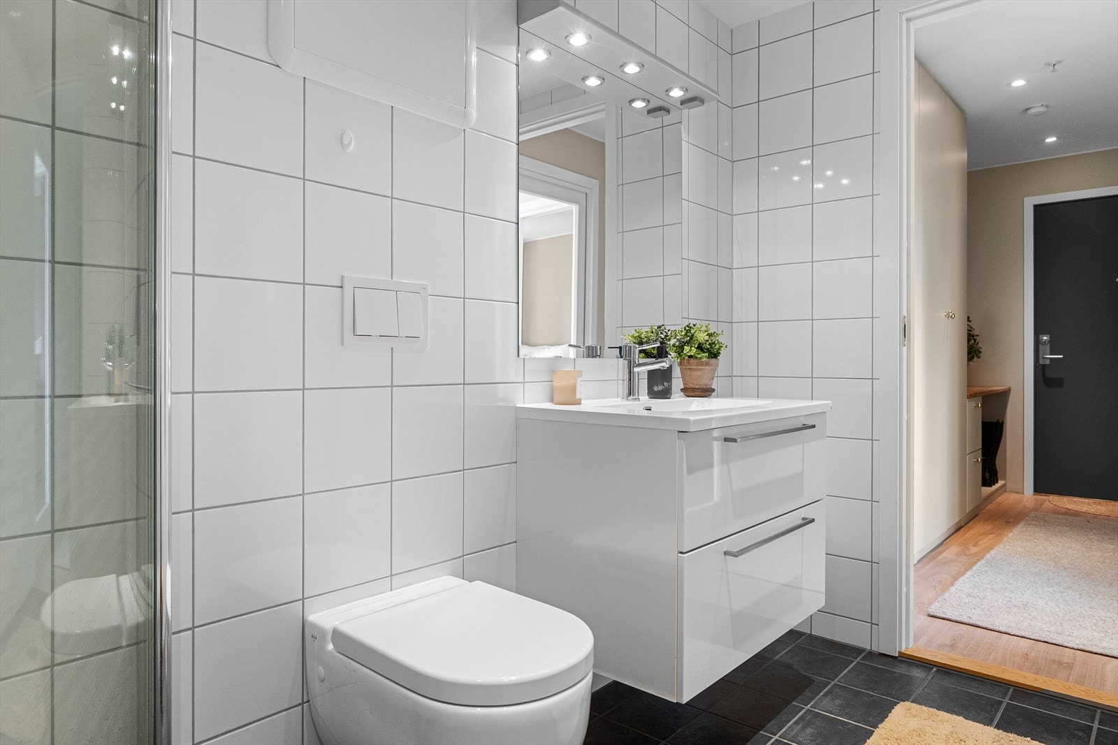 Badet er innredet med servant med skapinnredning, speil og lys over servant, vendbare dusjdører, vegghengt toalett og opplegg for vaskemaskin. Galleribilde