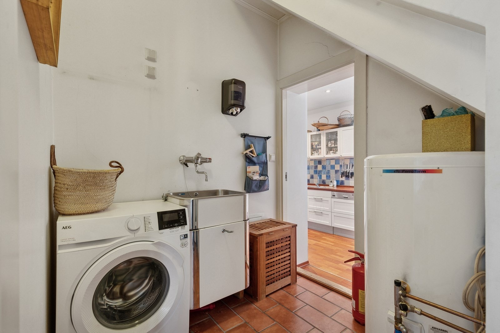 Praktisk vaskerom ved kjøkkenet, utstyrt med utslagsvask og varmtvannsbereder. Vaskemaskinen medfølger handelen. Galleribilde