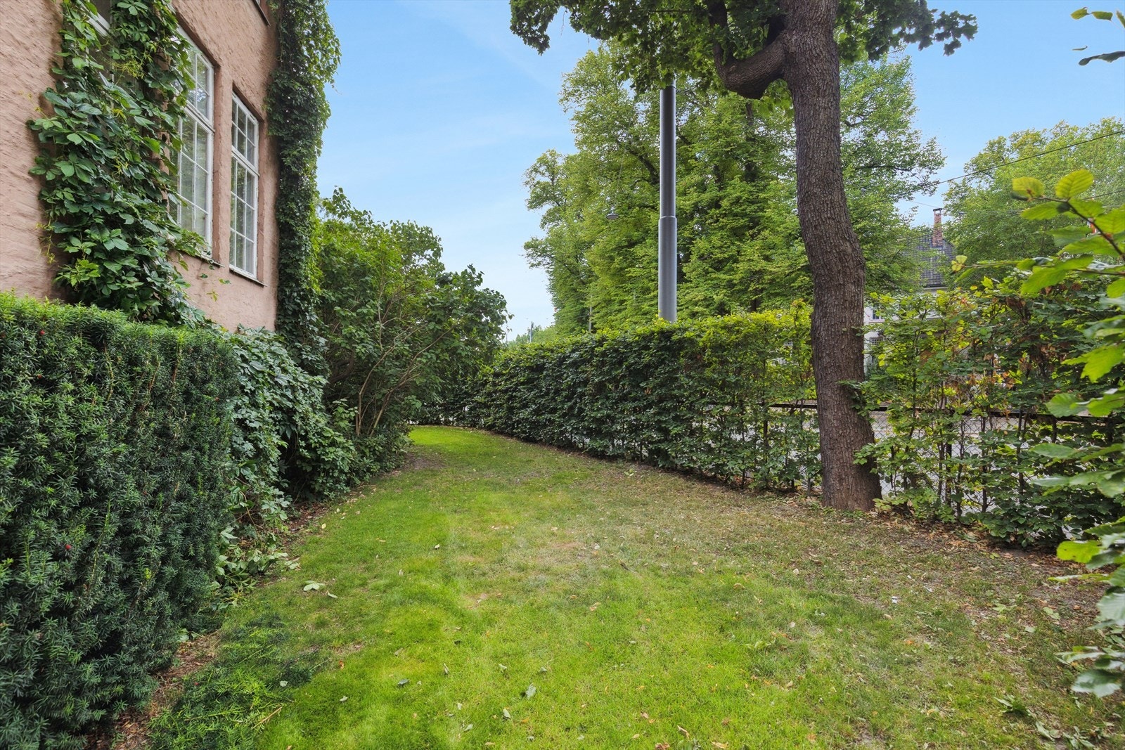 Fellesområdet fremstår som frodig og pent opparbeidet, med gressplen, trær og variert beplantning som skaper en hyggelig ramme rundt eiendommen. Galleribilde