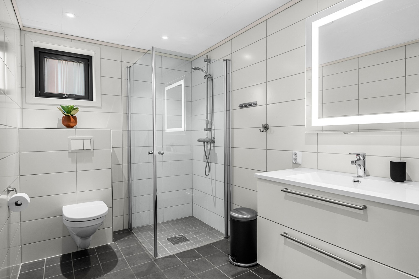 Lyst og tidløst flislagt bad med varmekabler i gulv, romslig dusjhjørne med regnfallsdusj og stor innredning Galleribilde