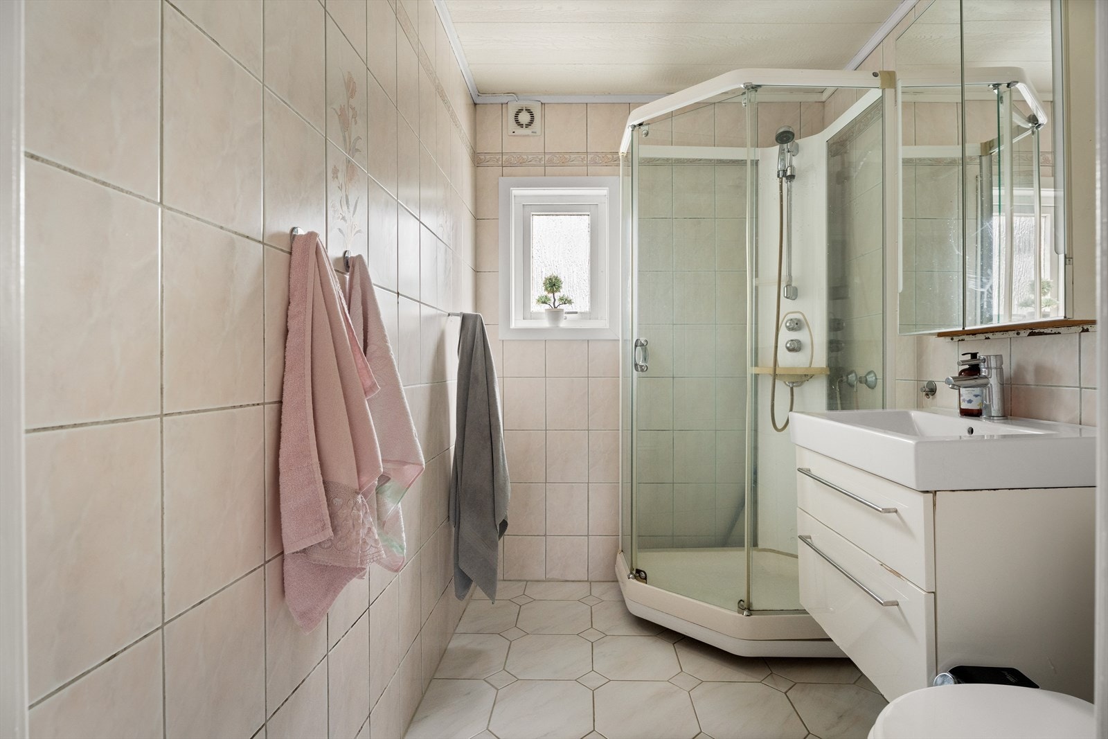 Badet i 1. etasje er av ukjent alder og har fliser på vegger og gulv samt malte plater i himling. Det er innredet med dusjkabinett, servantinnredning og toalett Galleribilde