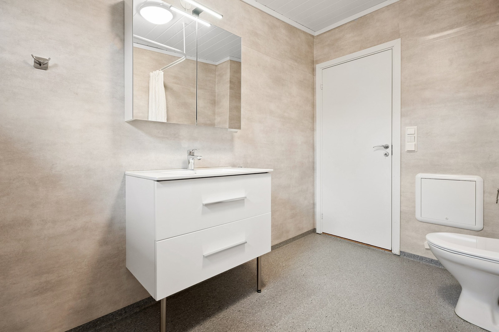 Badet er innredet med servant med underskap, et gulvmontert toalett og en dusj med forheng. Galleribilde