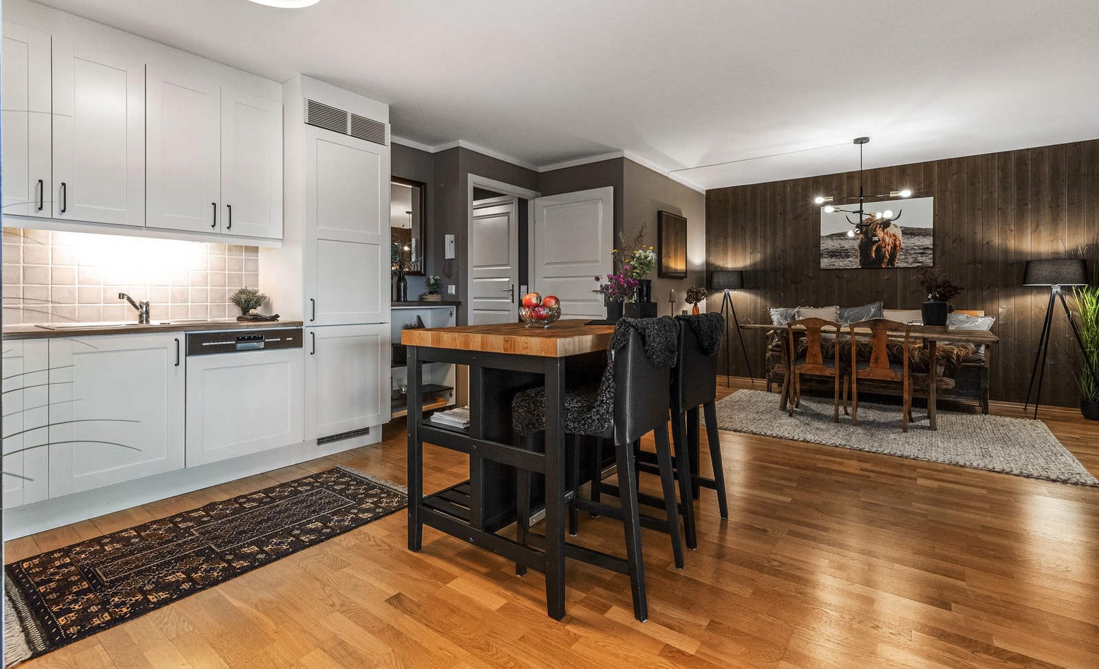 Kjøkkenet er lyst og inkluderende med sorte håndtak og integrerte hvitevarer som kjøl/frys, oppvaskmaskin, komfyr og koketopp Galleribilde