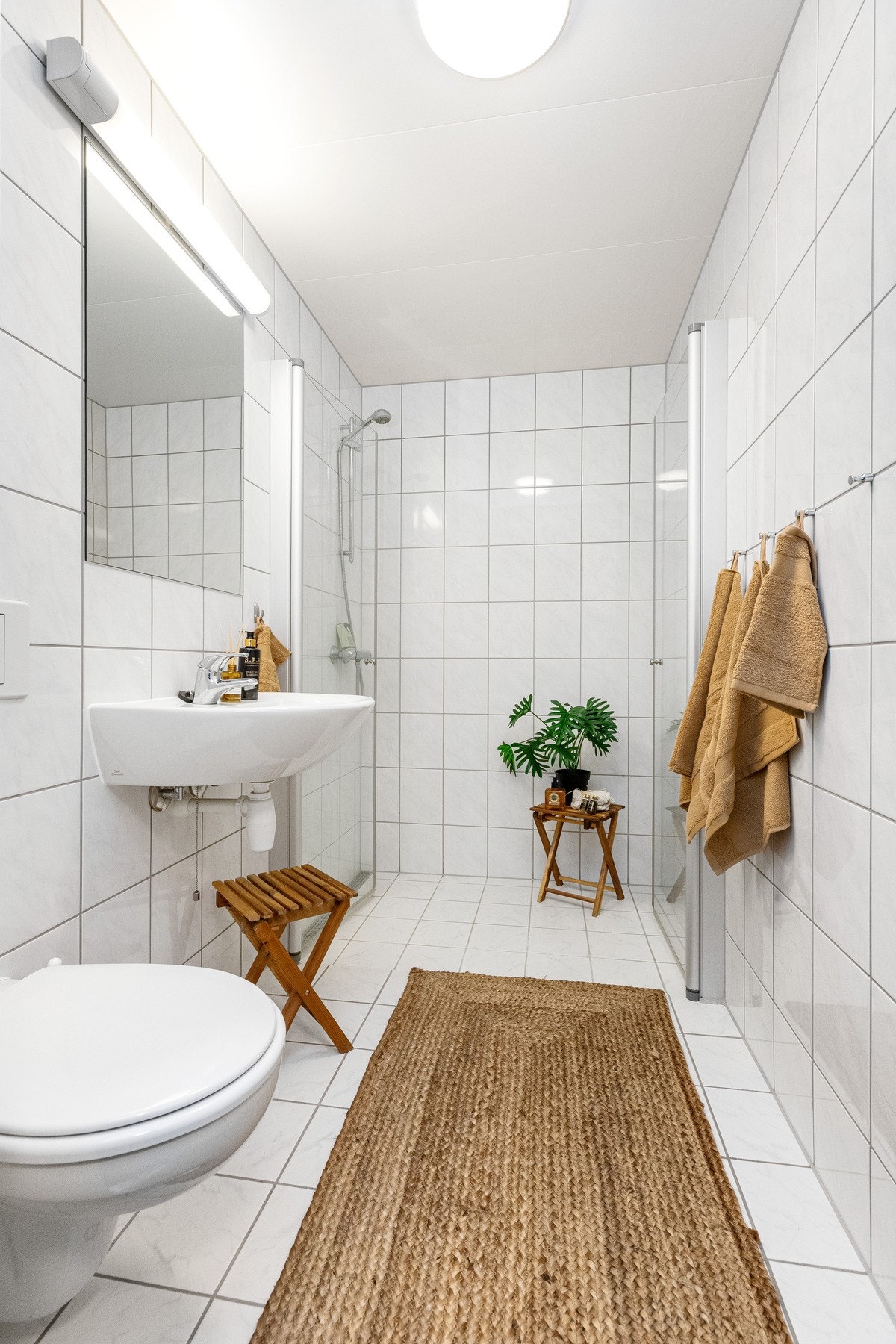 Bad nummer to har også lyse fliser, inkludert en romslig dusjnisje med glassdører på to sider, samt vegghengt servant og toalett Galleribilde