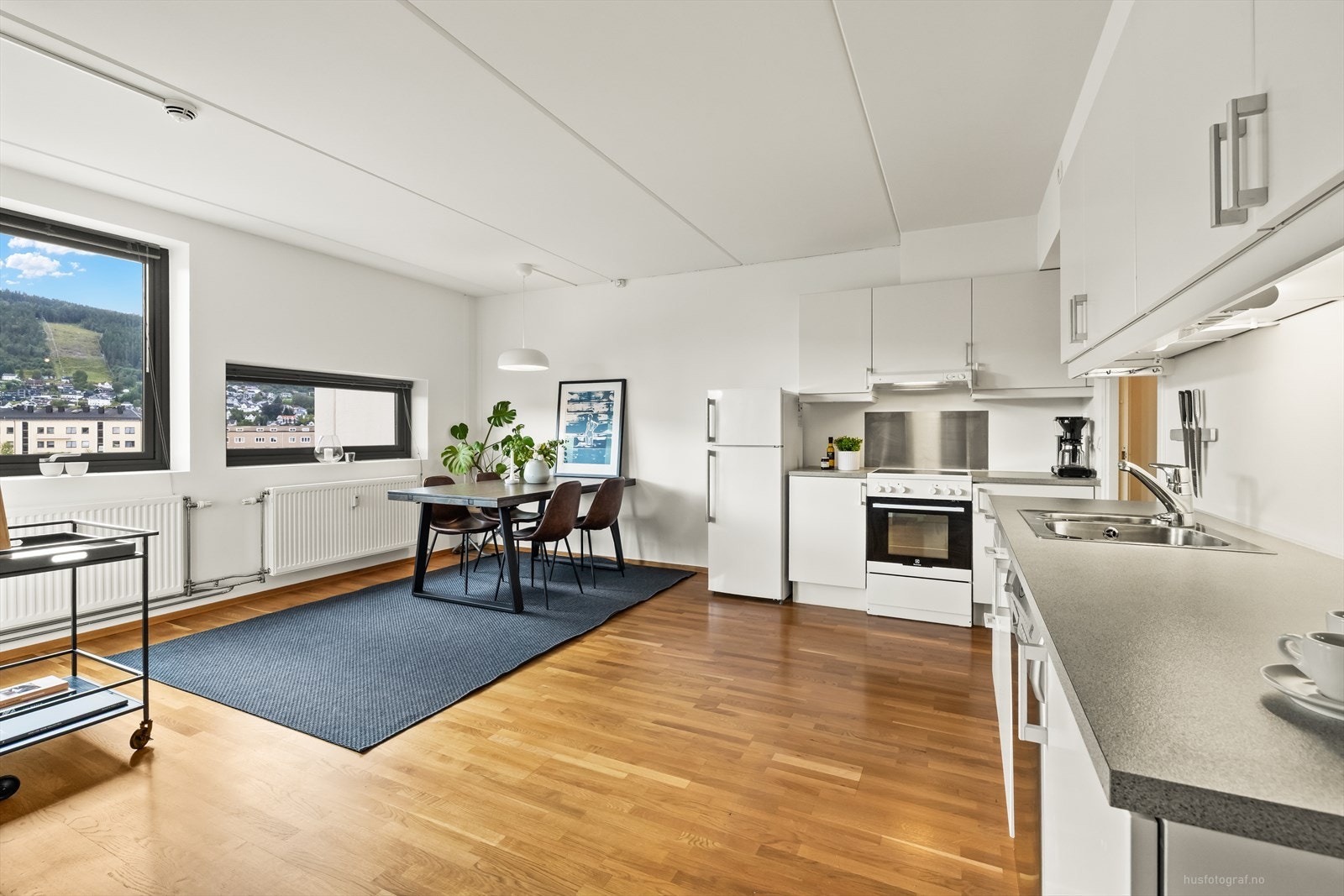 Hvit glatt kjøkkeninnredning og avtrekksvifte over komfyr. Røropplegg til oppvaskmaskin. Galleribilde