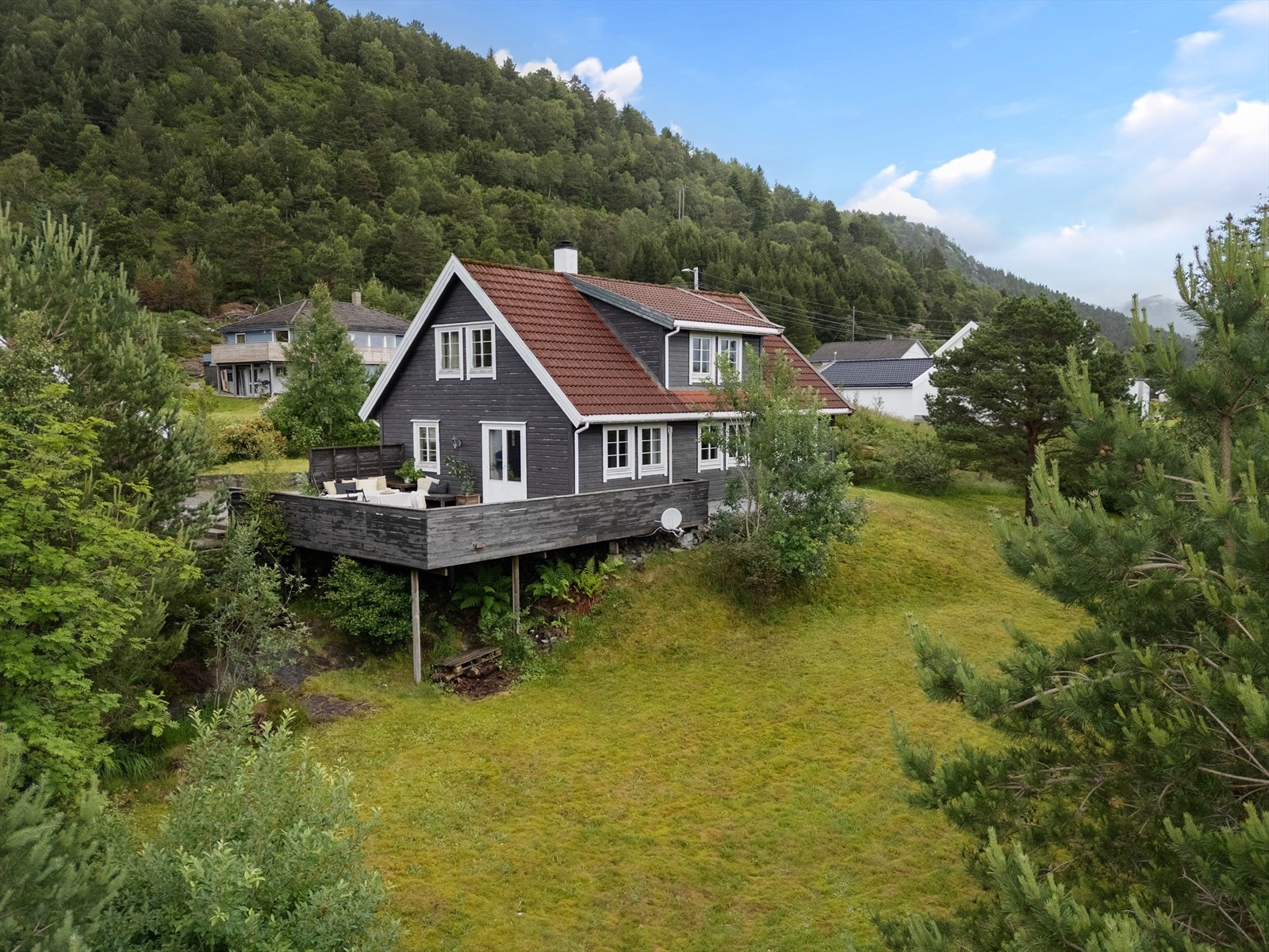 Tomten er pent opparbeidet med beplantning, treterrasse og plen. Galleribilde