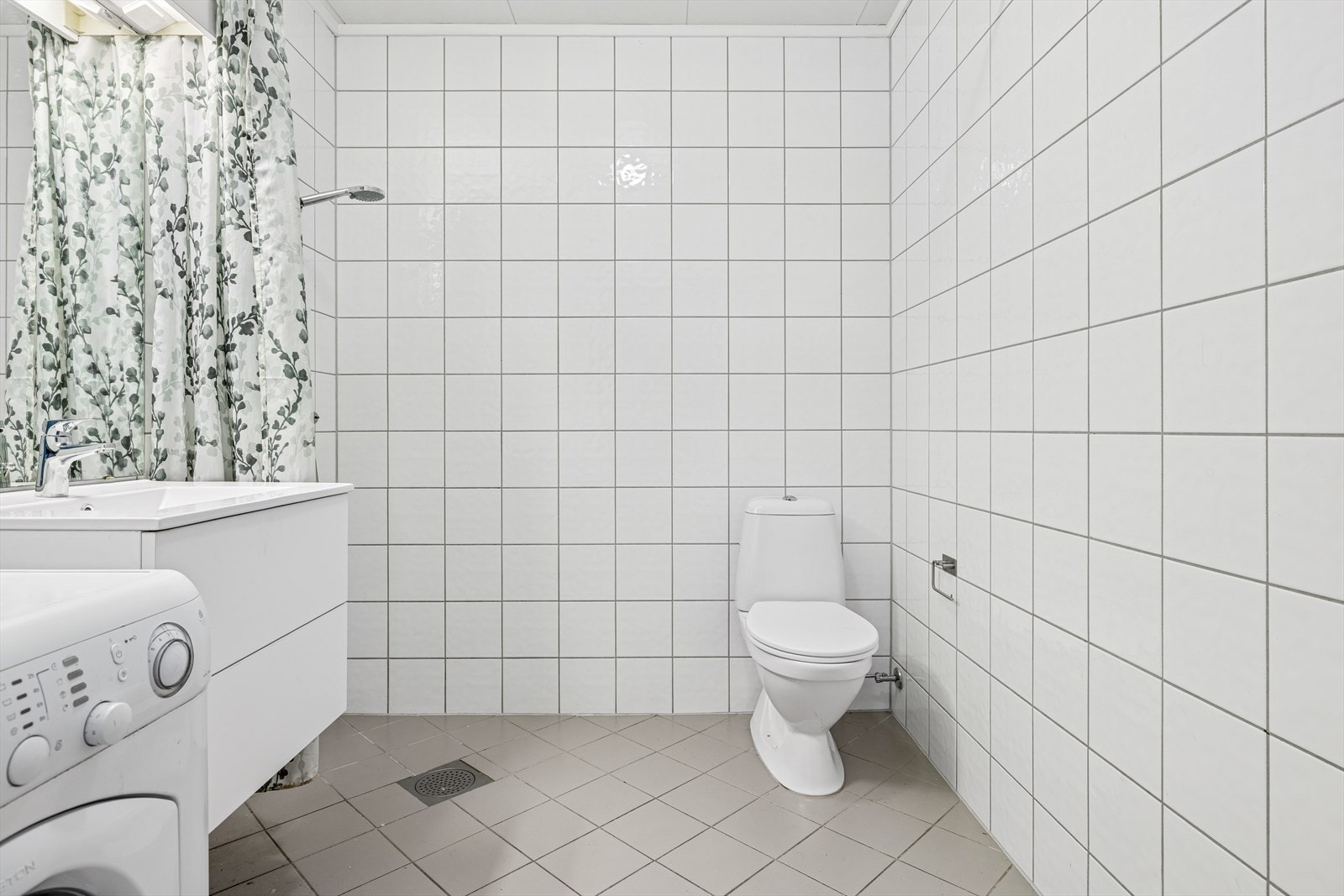 Videre er rommet utstyrt med baderomsinnredning med nedfelt servant, dusj med forheng og toalett. Det er opplegg for vaskemaskin her og elektriske varmekabler i gulvet. Galleribilde