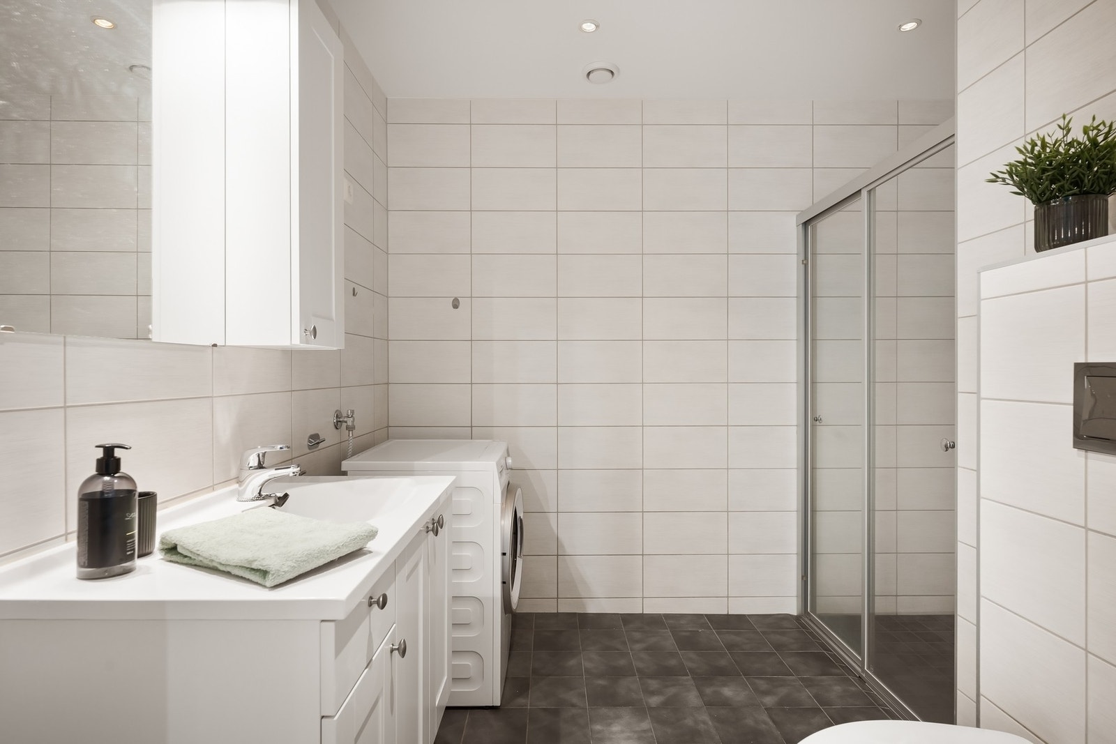 Badet er innredet med servantskap, vegghengt wc, speil, dusjhjørne og opplegg for vaskemaskin Galleribilde