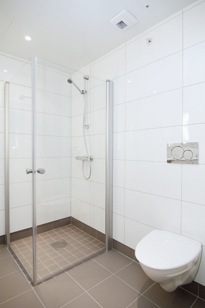 Badet er innredet med vegghengt toalett, dusjhjørne med glassdører og servant med over- og underskap Galleribilde
