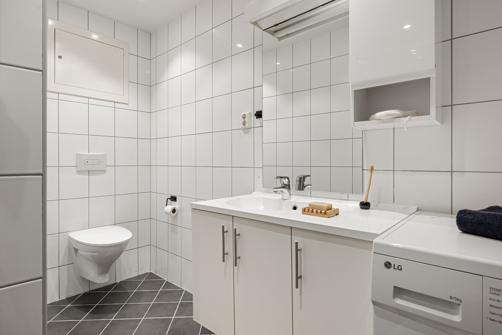 Badet fremstår lyst, tidløst og moderne. Av innredning inneholder badet Dusjnisje m/skyvedører, vegghengt toalett, opplegg for vaskemaskin og en praktisk baderomsinnredning. Galleribilde