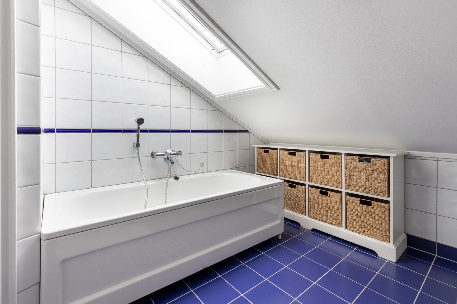 Rommet har varmekabler, flislagte overflater og hvitmalt skråtak. Galleribilde