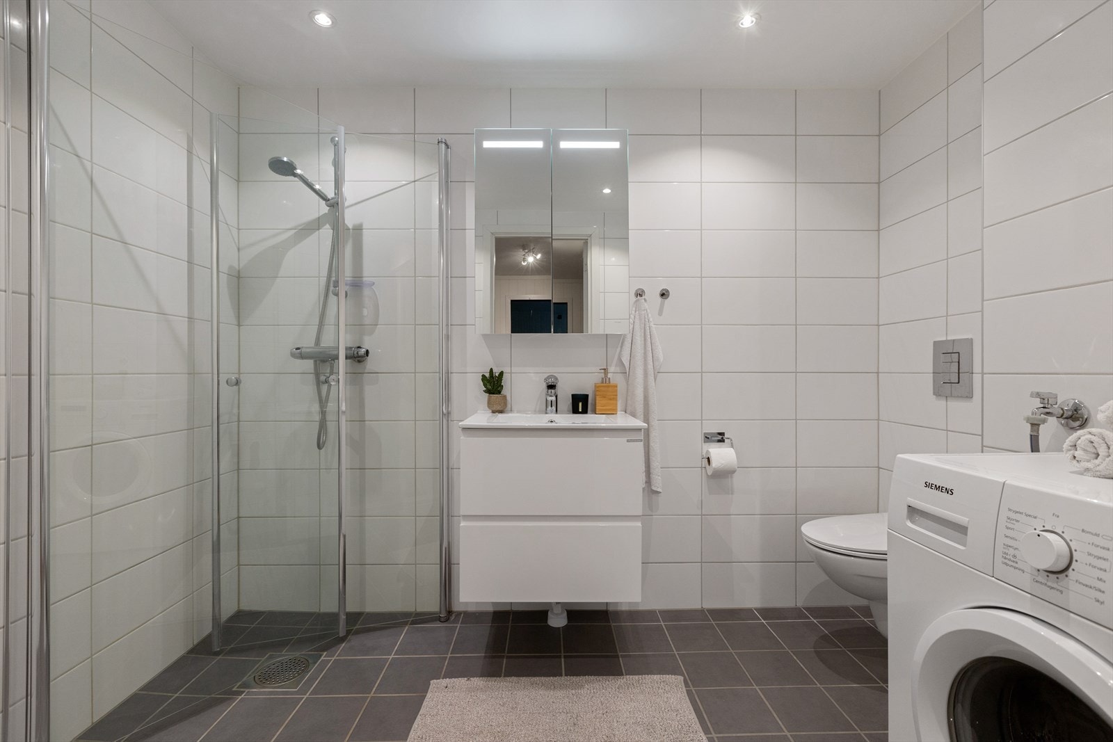 Flislagt bad med dusjhjørne og servant med underskap og overskap med speil Galleribilde