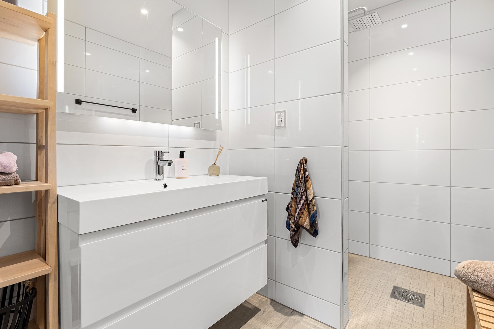 Innredet med servantinnredning, speil med lys på vegg over servant, vegghengt toalett og dusjhjørne. Galleribilde