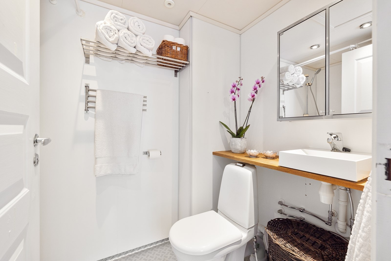 Praktisk baderomsinnredning med servant på benkeplate i heltre, speilskap, dusjnisje, klosett og opplegg for vaskemaskin. Galleribilde