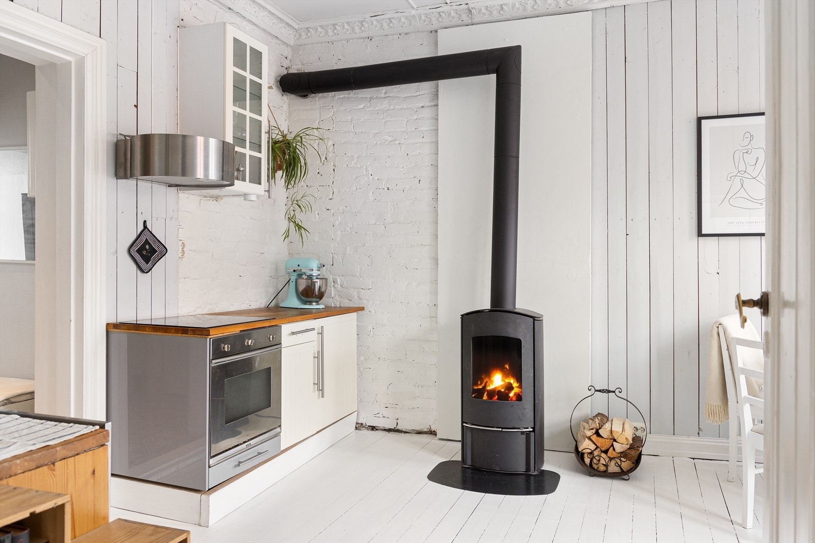 Kjøkkeninnredningen fremstår med lyse profilerte/glatte fronter, overskap med fronter i glass, benkeplater i heltre, oppvaskkum i porselen ventilator med kullfilter og integrerte hvitevarer. Galleribilde