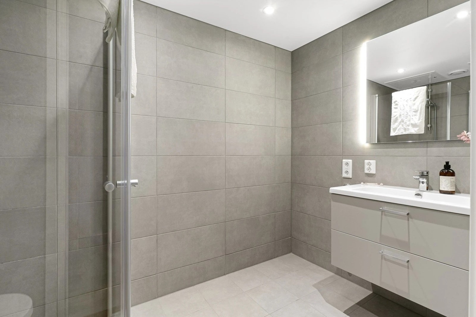 Lekkert bad med store fliser i naturtoner og varme i gulvet. Galleribilde