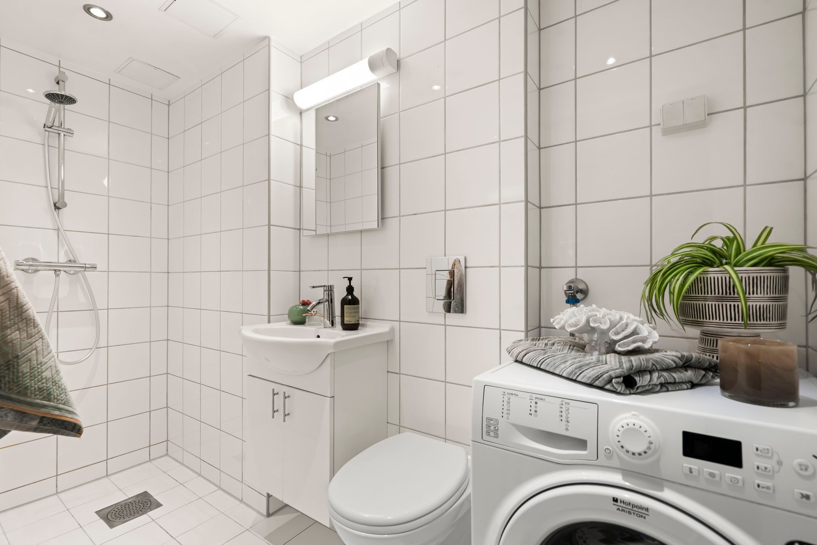 Lyst og delikat baderom fra 2010 med hvite gulv- og veggfliser. Badet er innredet med servant med lys innredning med skuffer, speilskap, toalett og dusj med nytt dusjarmatur i 2025. Galleribilde