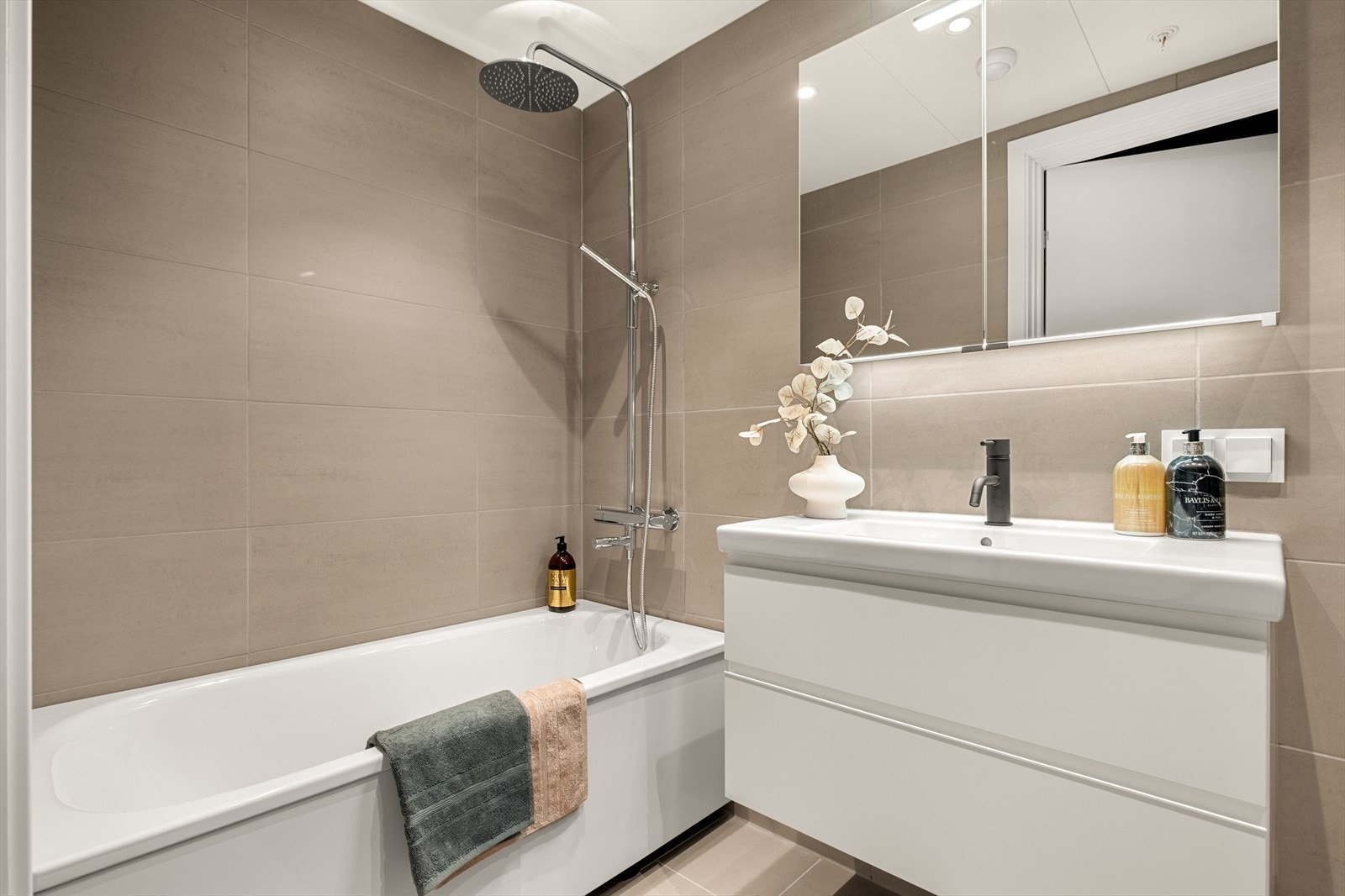 Badet er innredet med dusjbadekar, baderomsinnredning med speilskap og servant, opplegg for vaskemaskin, veggmontert wc og downlights Galleribilde