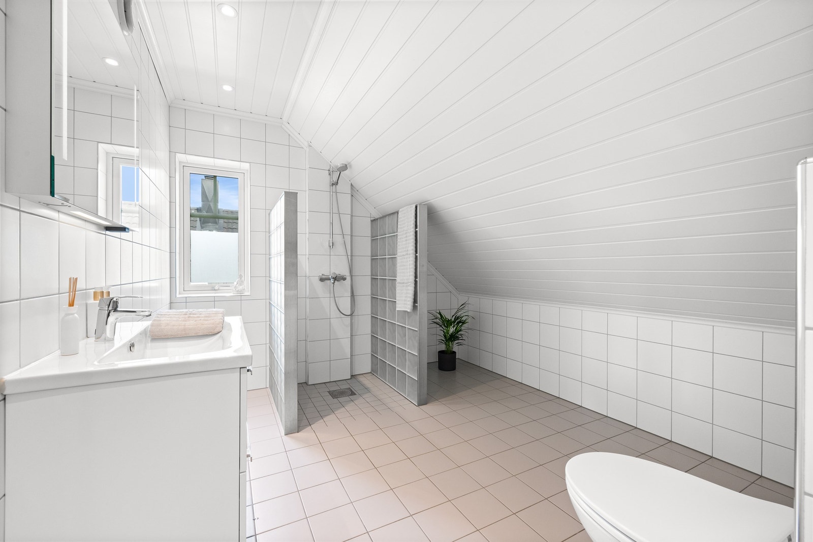 Badet på loftet er også flislagt med varme i gulv. Innredningen består av servant, speil med belysning, vegghengt toalett, dusjnisje med vegger av glassbyggerstein Galleribilde