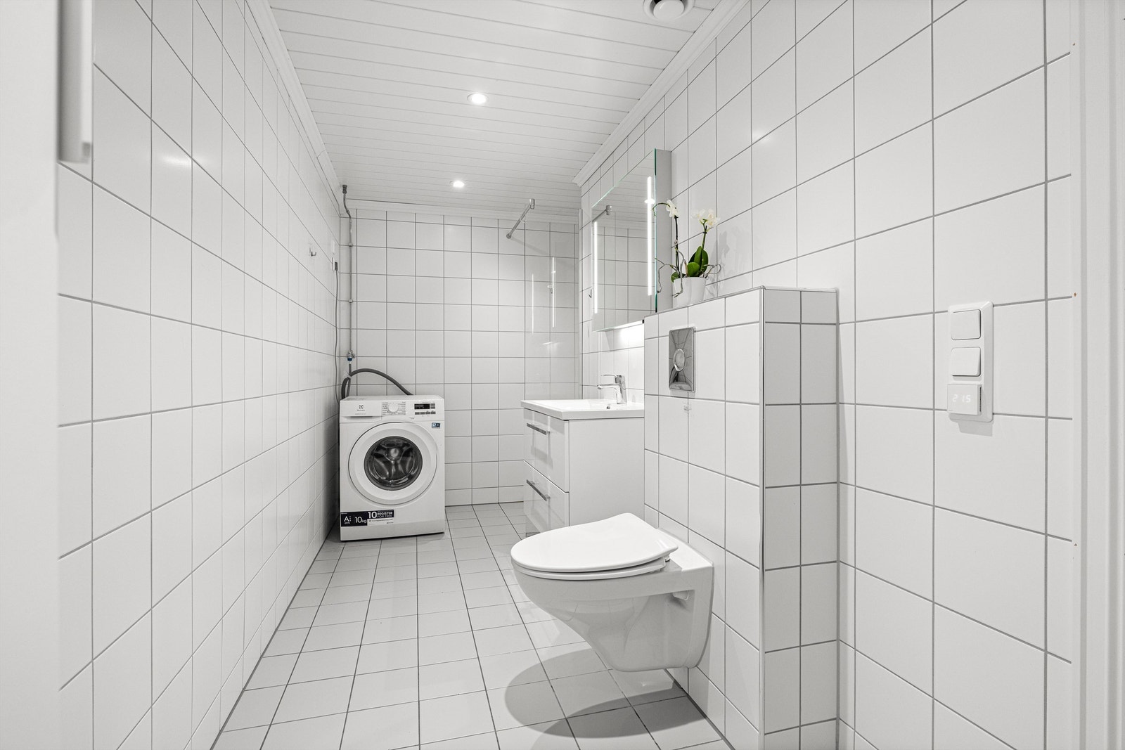 Flislagt baderom fra byggeår, med varme i gulv. Høyskap og innredning med speil med belysning, vegghengt toalett og dusjnisje. Opplegg for vaskemaskin Galleribilde