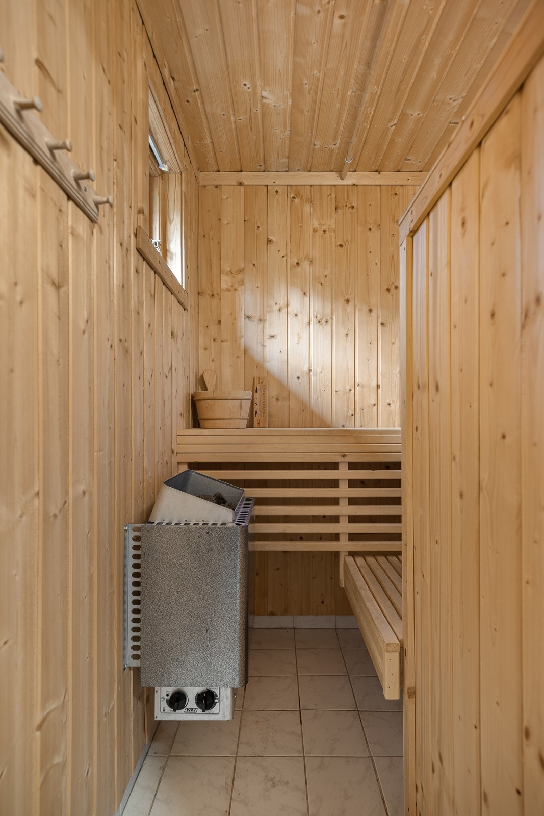 Badstuen har fastmonterte benker, elektrisk badstue ovn og flislagt gulv Galleribilde