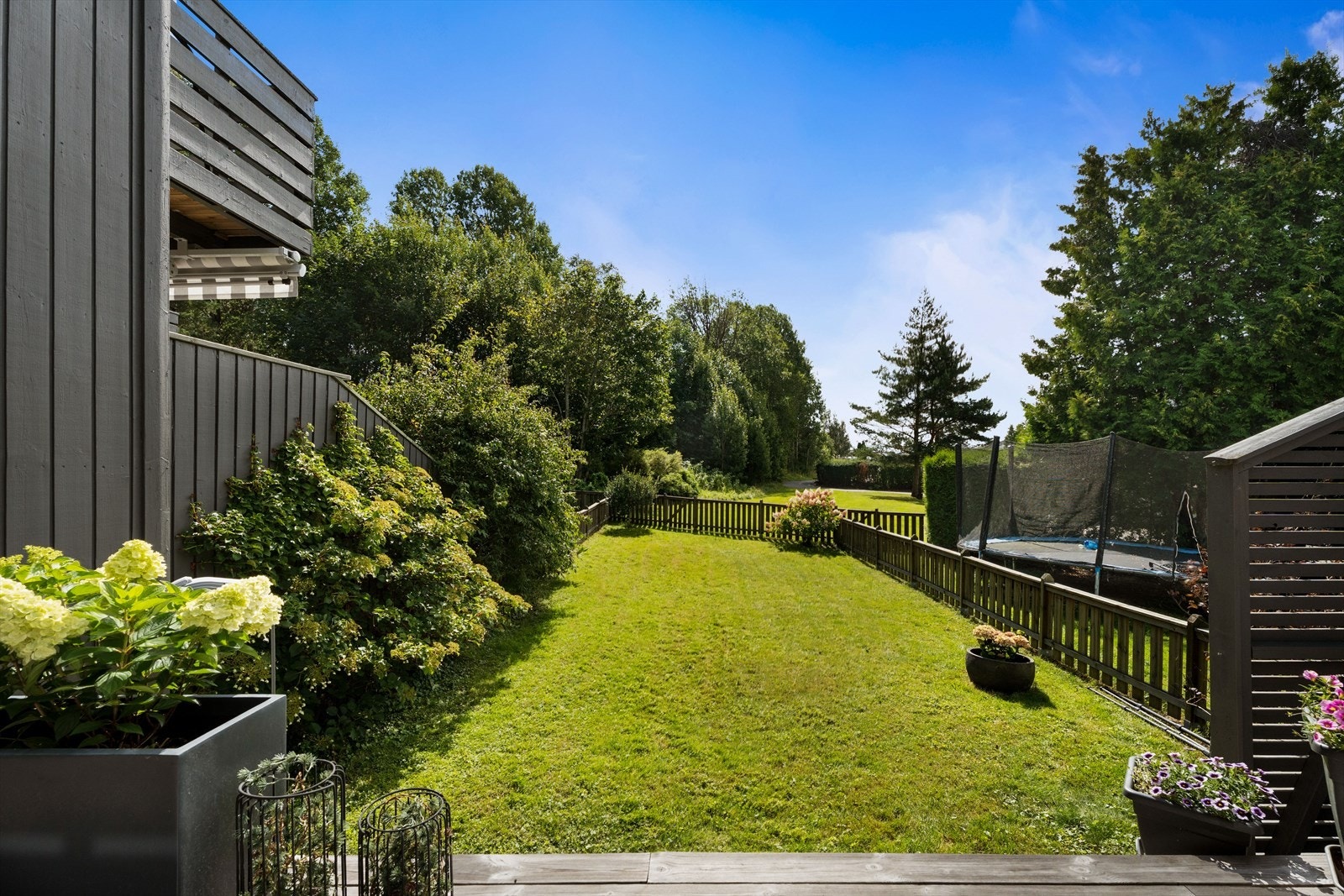 Tomten er pent opparbeidet med plen og beplantning av busker, noe som gir et grønt og trivelig utemiljø Galleribilde