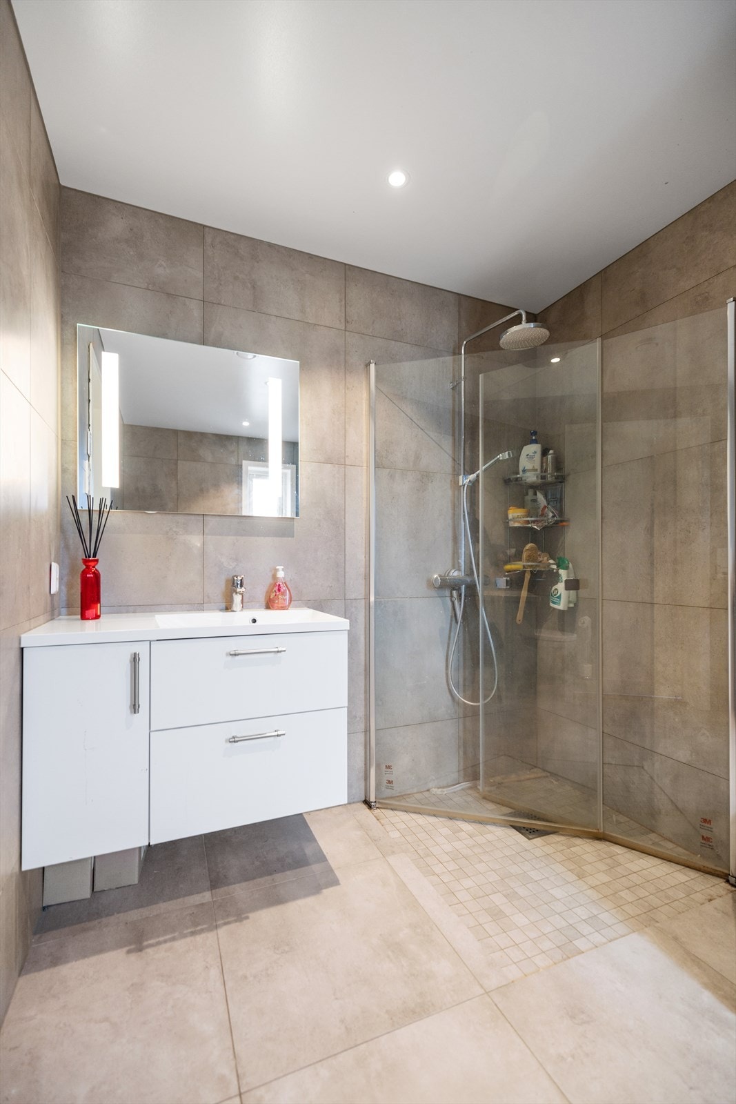 Det er montert innredning med hvite fronter og heldekkende servant, speil med integrert belysning, vegghengt toalett og dusjhjørne. Galleribilde