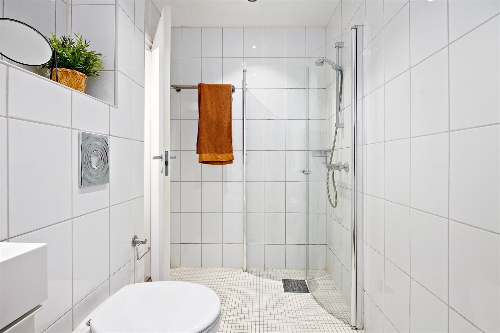 Flislagt bad med dusj med innfellbare glassdører, servant i helstøpt plate, veggmontert toalett og opplegg for vaskemaskin. Galleribilde