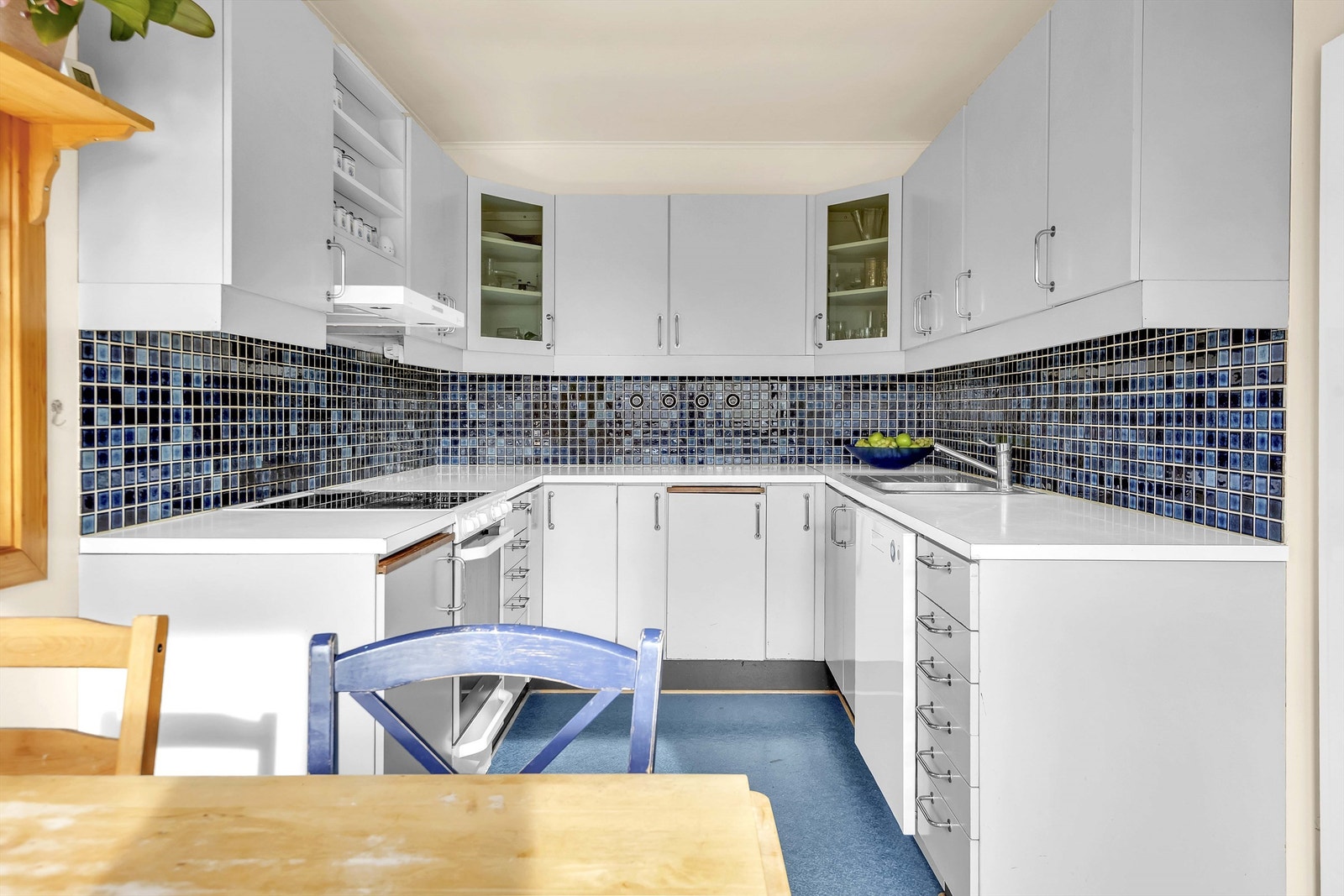 Kjøkkeninnredningen fra ukjent år med slette fronter, benkeplate i laminat med sponkjerne og oppvaskkum i stål med ett-greps blandebatteri. Det er ventilator med avtrekk ut, komfyr, oppvaskmaskin, kjøleskap og klessjakt ned til vaskerom kjeller via skap Galleribilde