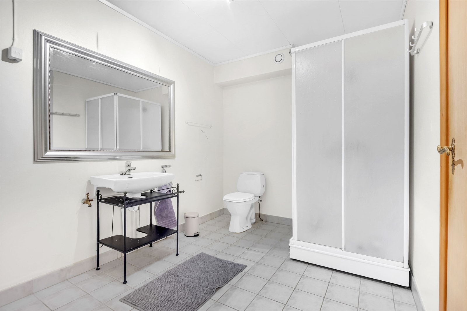 Baderom fra byggeår i hybel. Det er servant, speil, dusjkabinett og gulvmontert toalett. Videre så er det avtrekk og luftespalte ved terskel er vurdert som tilfredsstillende. Galleribilde