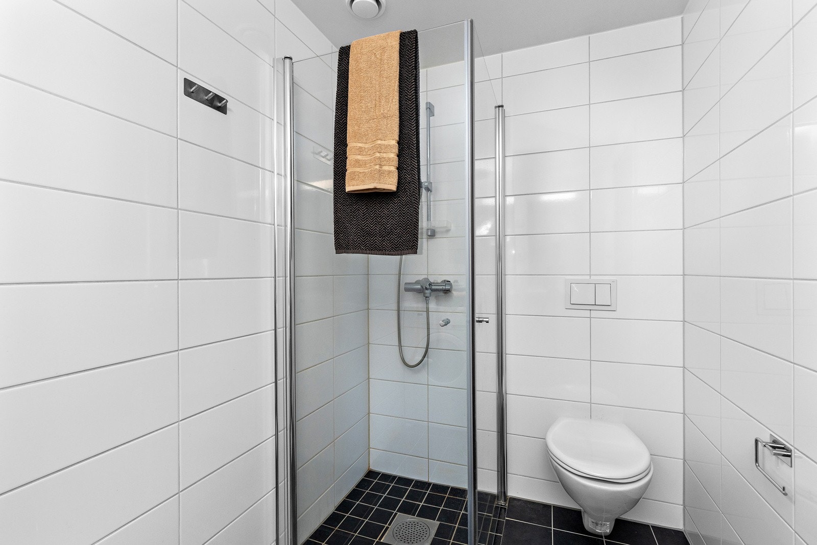 Tidløst bad med fliser på gulv og vegger. Badet er utstyrt med dusjhjørne med glassdører og vegghengt toalett Galleribilde