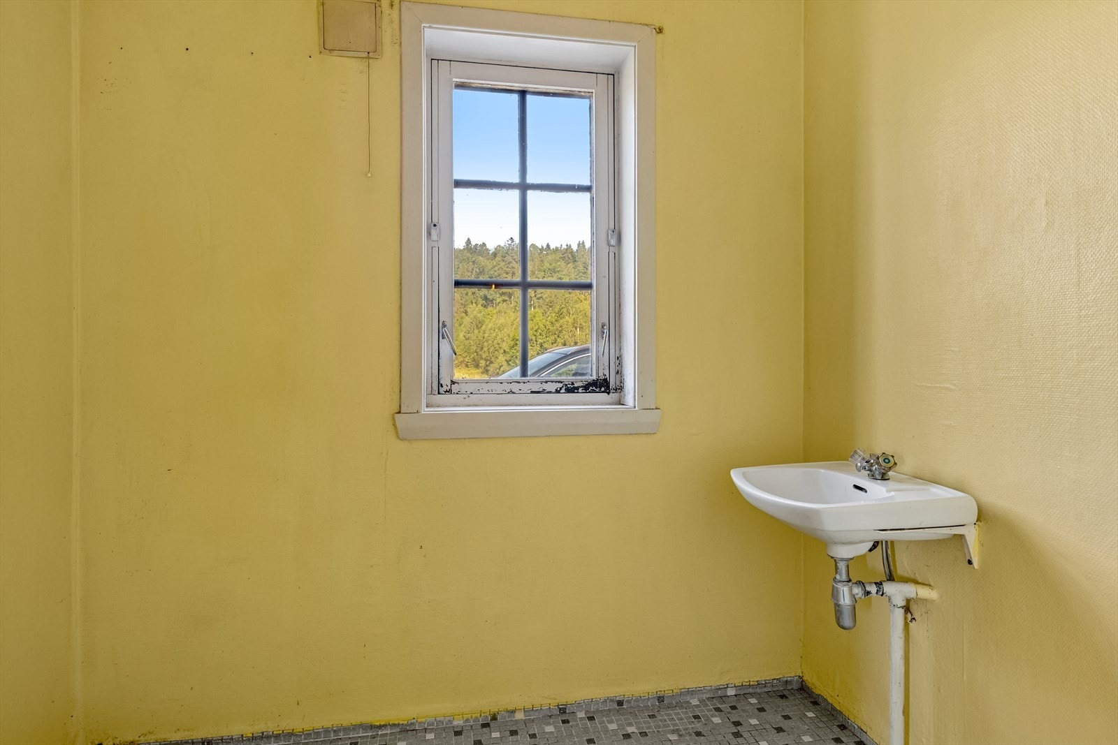 Bad/vaskerom i 1.etasje fra 1970-tallet med flislagt gulv på betong, vegger med malt strietapet og malte plater i himlingen. Rommet inneholder servant og opplegg for vaskemaskin. Våtrommet må oppgraderes for å tåle normal bruk etter dagens krav. Galleribilde