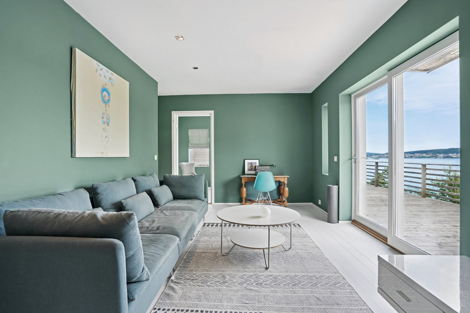 Vi beveger oss ned og her er det stue med skyvedør til terrasse og trapp til fellesområde ved sjøen Galleribilde