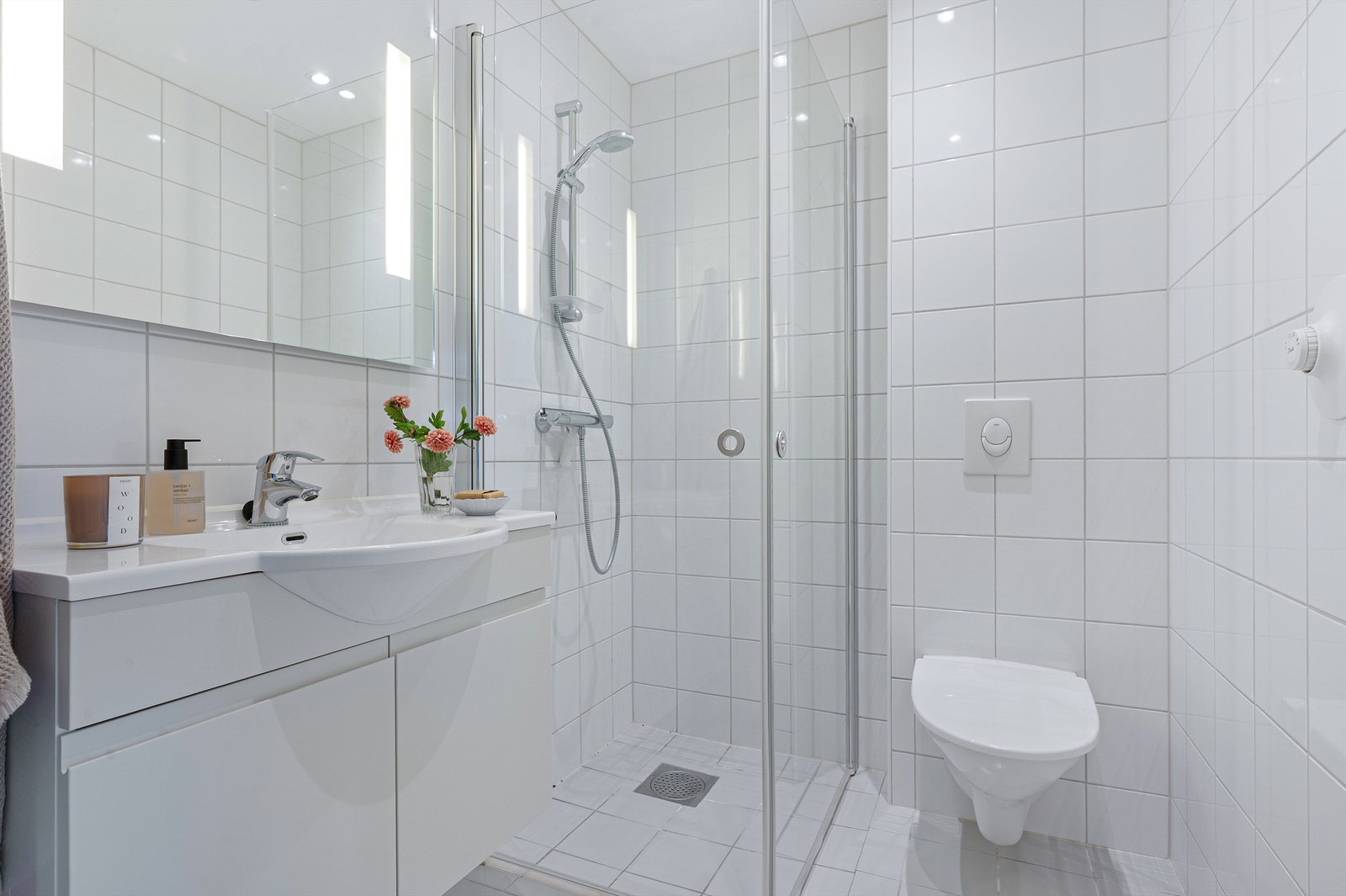 Lyst og moderne bad med flislagte overflater, vegghengt toalett, dusjhjørne med glassdører og stilfull innredning. Et praktisk og tidløst bad med god utnyttelse av plassen. Galleribilde