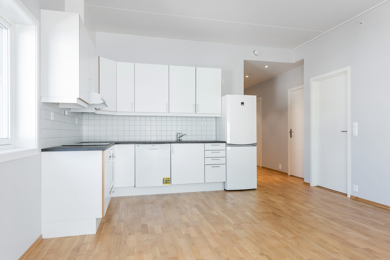 Kjøkken i åpen løsning med stue, hvor innredning er fra byggeår med under og overskap og fliser montert i benkerygg Galleribilde