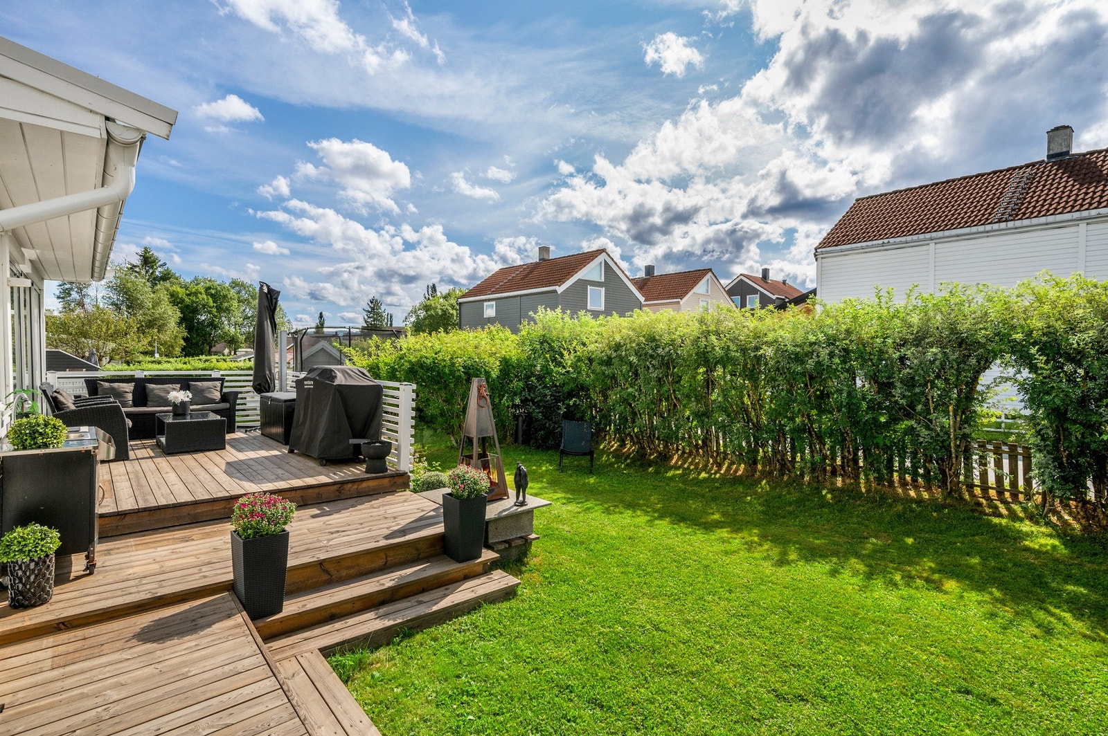 Uteområdet er pent opparbeidet med terrasser, plen og frodig hekk Galleribilde