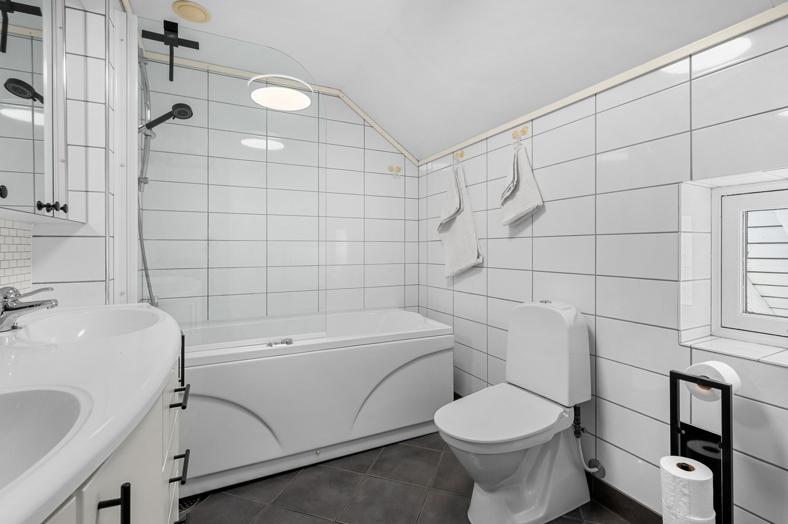 Lyst og delikat baderom med kombinert badekar og dusj Galleribilde